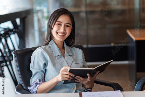Happy smiling businesswoman holding a book sitting in a chair. Looking at the camera. © amnaj