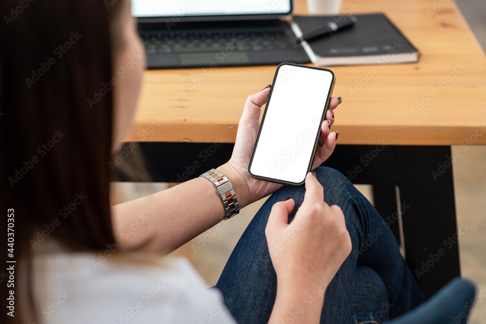 © amnaj - Close-up view of a woman hand using a smartphone with a blank white screen at the office. © amnaj - Close-up view of a woman hand using a smartphone with a blank white screen at the office.