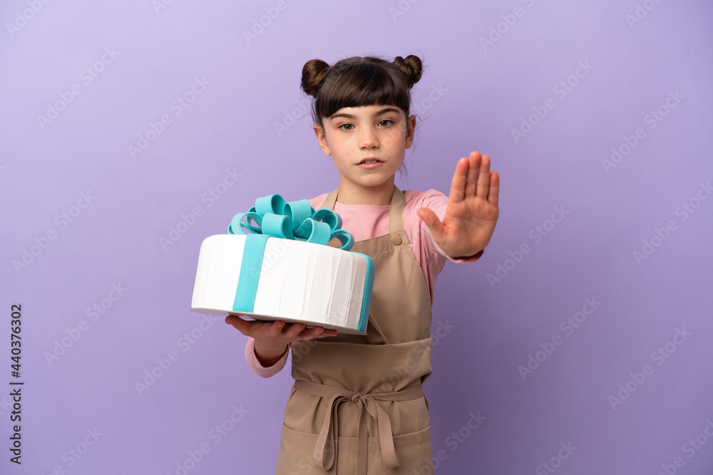 Pastry little girl holding a big cake isolated on purple background making stop gesture Pastry little girl holding a big cake isolated on purple background making stop gesture