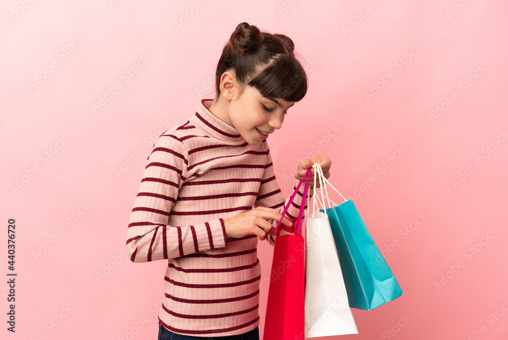 Little caucasian girl isolated on pink background holding shopping bags