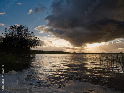 Sunset sky over a lake surface. River Corrib  Galway city  Ireland. Dark and dramatic scene. Sun flare and reflection in the water