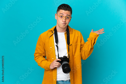 Young caucasian photographer man isolated on blue background having doubts while raising hands