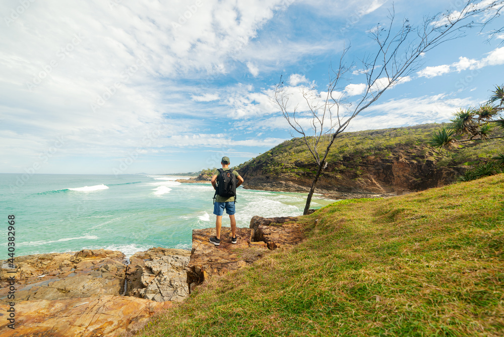Fototapeta premium Man Standing on Cliff Looking at Seashore in Summer in Noosa, Queensland, Australia.Explorer Concept