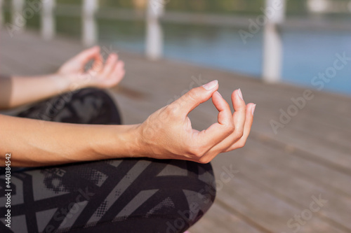 Close-up of hands of a young woman who meditates while holding fingers in yoga sign sitting on the sea pier. Peaceful girl keeps hands in mudra gesture sitting in the lotus pose
