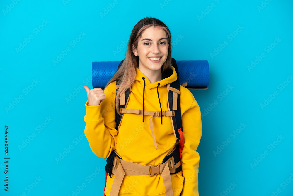 Young mountaineer woman with a big backpack isolated on blue background pointing to the side to present a product Young mountaineer woman with a big backpack isolated on blue background pointing to the side to present a product