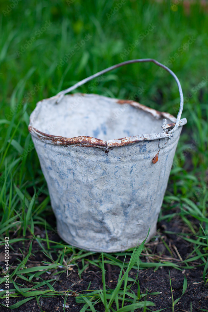 large vertical photo. summer time. old metal bucket with rust around the edges against a background of green grass. farm watering tools. eco materials. large vertical photo. summer time. old metal bucket with rust around the edges against a background of green grass. farm watering tools. eco materials.