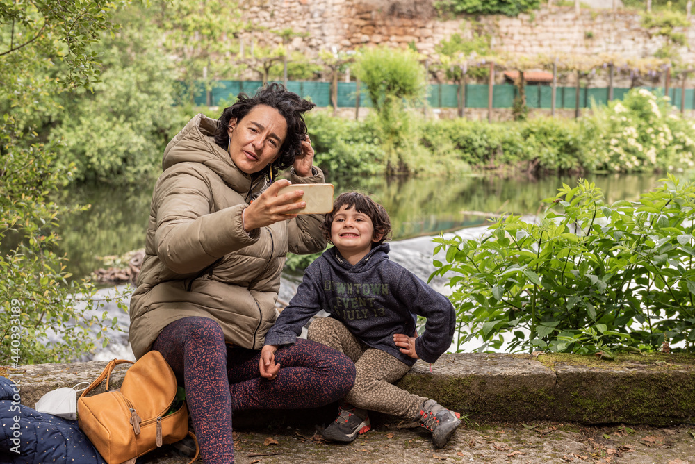 mother and her daughter taking a selfie sitting next to a river mother and her daughter taking a selfie sitting next to a river