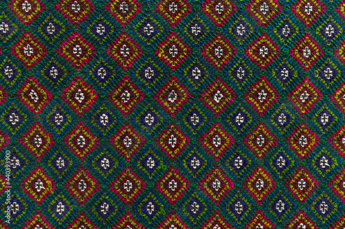 Close up view to the green and red carpet with square old patterns. Grange handmade wool texture.