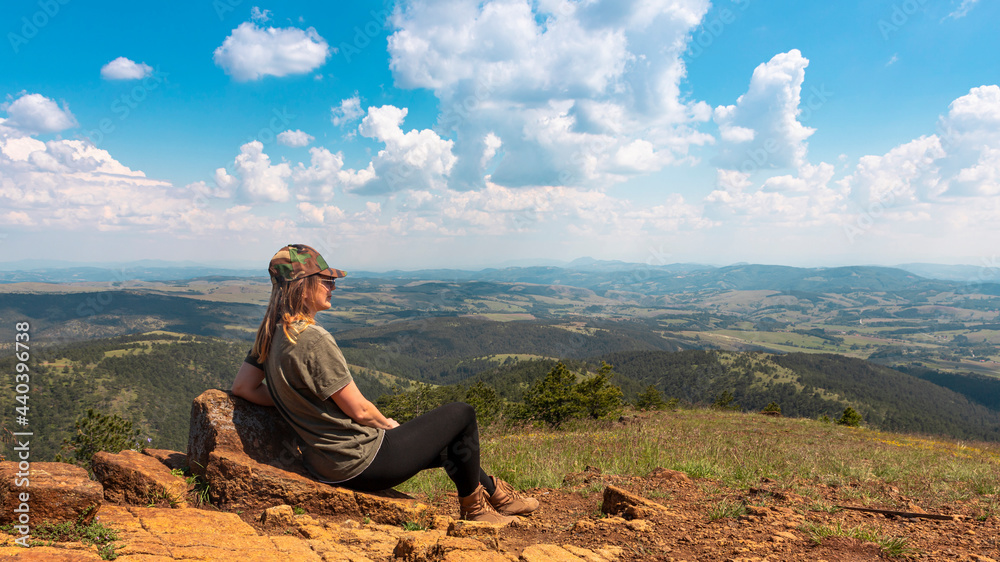 Tourist girl hiker resting at the top of the mountain and enjoying amazing landscape view of mountains and beautiful sky