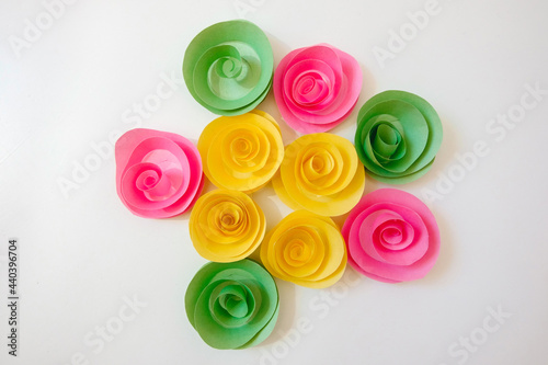 A group of paper flowers (yellow, green, pink) lies on a light background. View from above. Isolated. Romantic concept