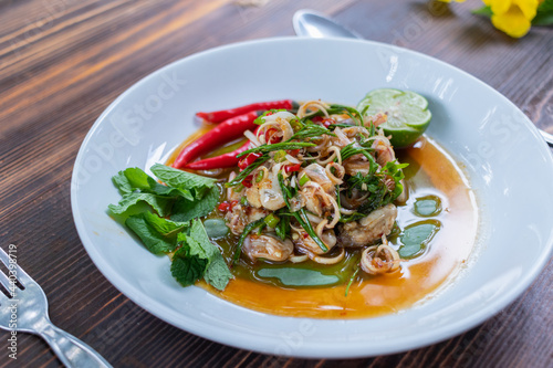 Fresh oysters are served in a white plate and topped with a spicy Thai-style sauce, also known as "Yum Oysters", with a spicy taste from fresh chili and sour lime. It is a popular and delicious dish.