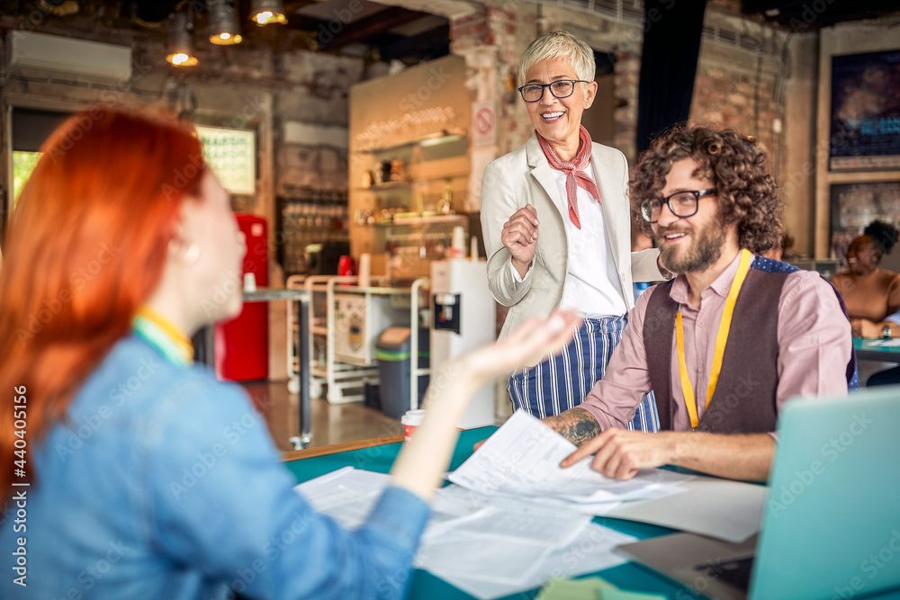 Elderly female boss is talking to her young colleagues in the office. Employees, office, work Elderly female boss is talking to her young colleagues in the office. Employees, office, work