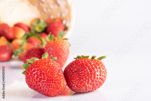 Fototapeta Naklejka Na Ścianę i Meble -  Strawberries, beautiful strawberries dropped from a straw braided basket onto a white surface, selective focus.