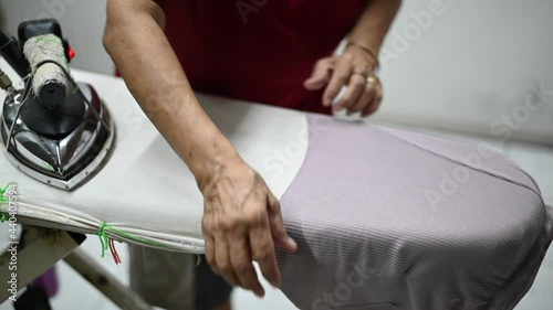 An Asian elderly woman who is a housewife folding clothes at the laundry for ironing. photo