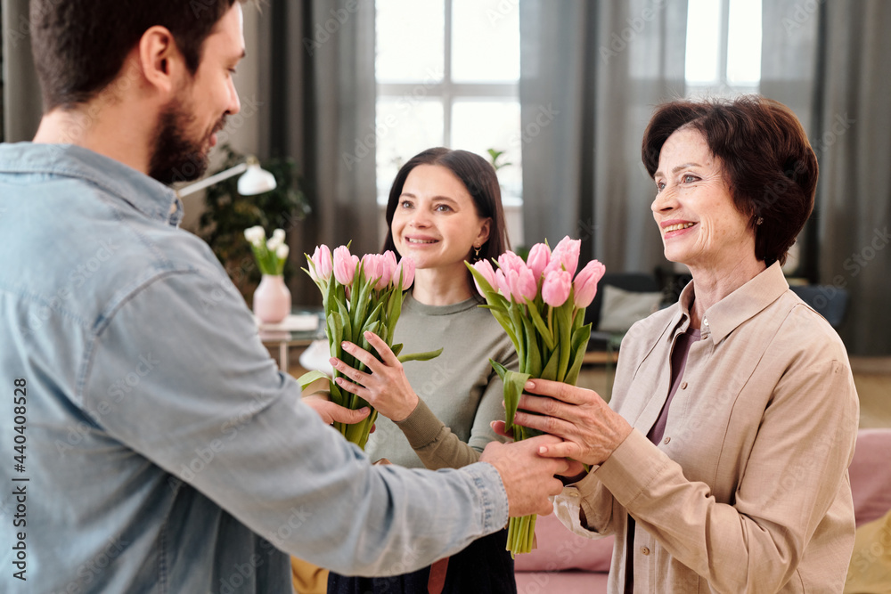 Cheerful females with tulips looking at kind young man Cheerful females with tulips looking at kind young man
