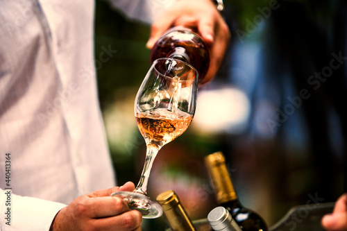 The waiter serves rose, red and white wine from the wine bottle in the wine glass at an event.