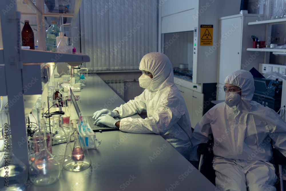 Female scientist in wheelchair looking at laptop display by her colleague during work in laboratory