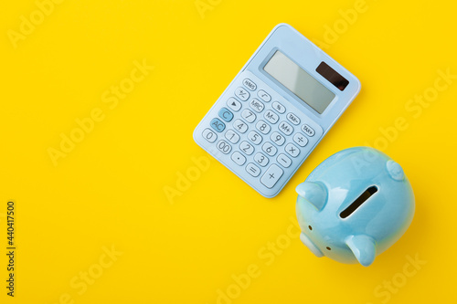 Piggy bank with calculator on yellow background