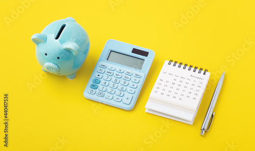 Calculator with calendar and piggy bank on yellow background