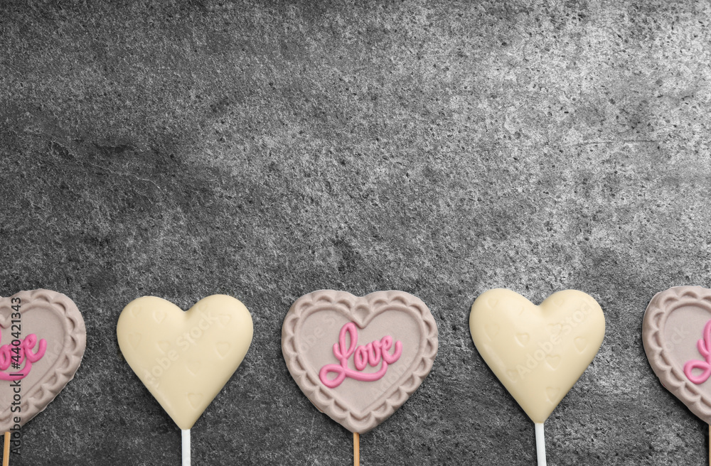 Different chocolate heart shaped lollipops on grey table, flat lay. Space for text Different chocolate heart shaped lollipops on grey table, flat lay. Space for text