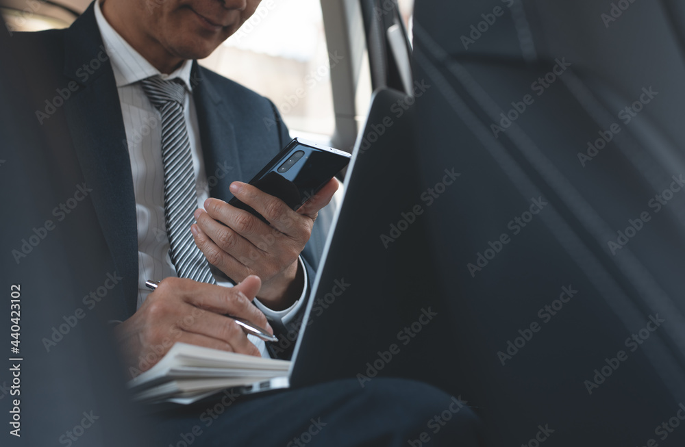 Businessman working on laptop computer and using mobile phone inside a car, portable office concept