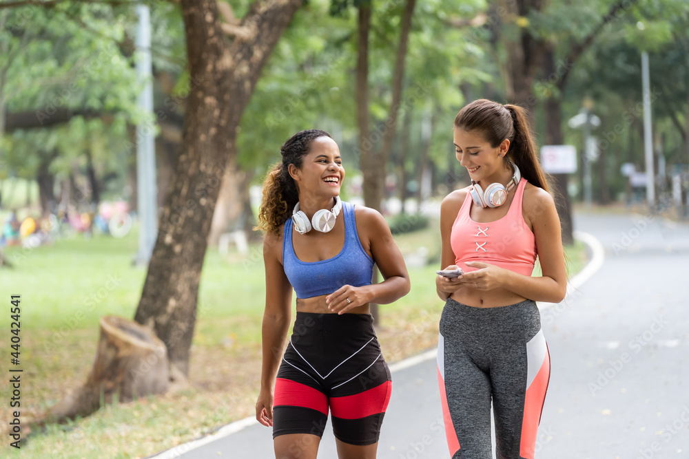 Fototapeta premium Young Women friends jogging together at park. Female runners listening to music while jogging.