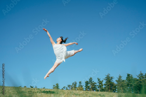 空と白いワンピースの踊る女性（ジャンプ）  © buritora