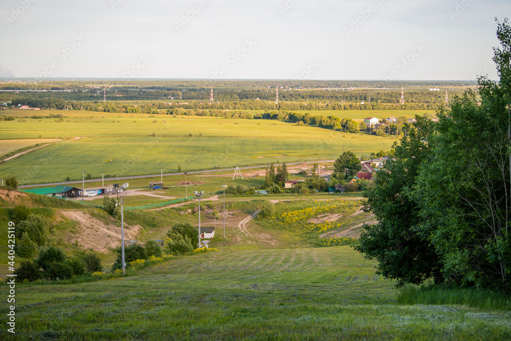 Panoramic view from the mountain to small rural settlement among fields and forests at sunset in summer.