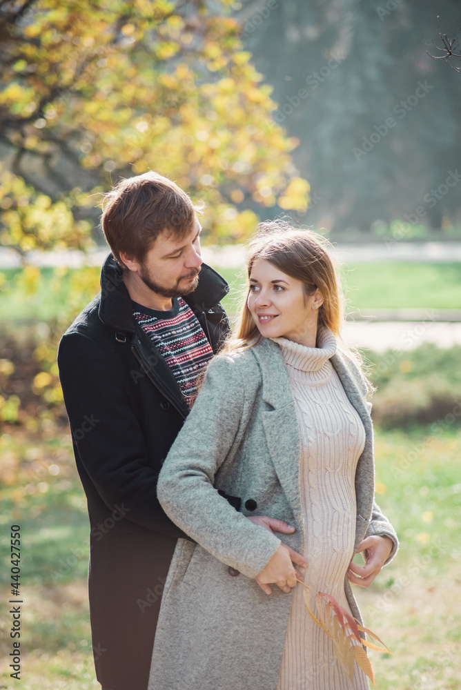Fototapeta premium Family together in autumn park. Happy couple Husband and his pregnant wife relaxing in nature. happy married couple expecting baby. Pregnancy, maternity concept. Parents hands on pregnant belly