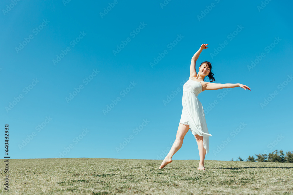 空と白いワンピースの踊る女性
