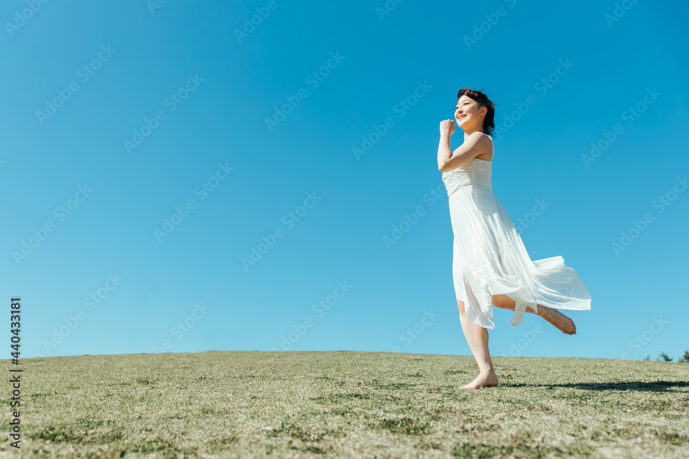 空と白いワンピースの走る女性
