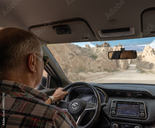 hispanic senior man driving a car on a dirt road between mountains - travel concept