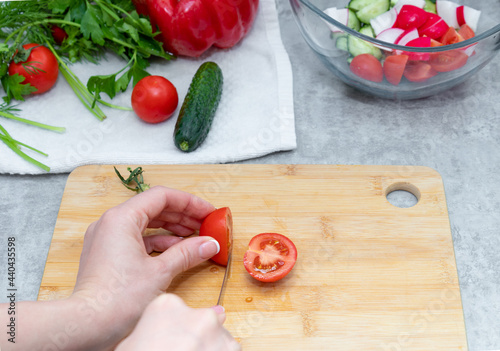 Cutting of tomatoes on the board in home kitchen. Preparation of the fresh vegetables salad.