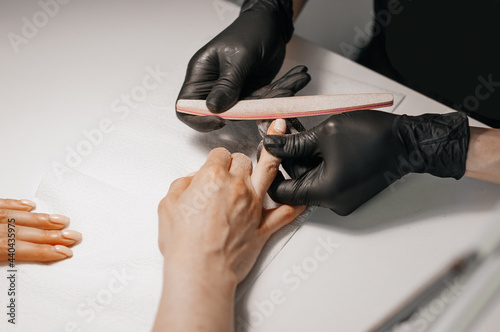 Manicurist filing client s nails at table  closeup. Spa treatment. Beautician filing female clients nails