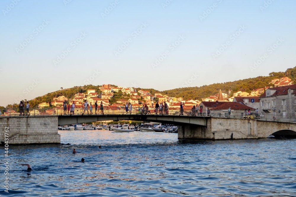 A view of the bridge connecting the mainland of Trogir to the island of Ciovo along the Croatian coast.  It is near sundown and people are jumping into sea below.