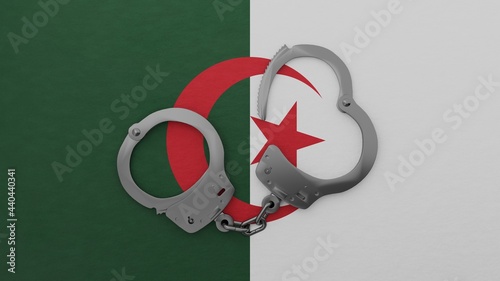 A half opened steel handcuff in center on top of the national flag of Algeria