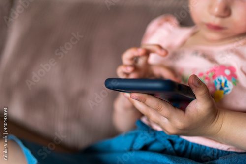 girl with blond hair plays with a smartphone at home. child and smartphone in hands. children with digital tablet