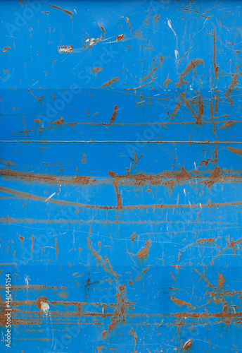 Close-up of a weathered sheet metal plate painted in blue. Paint is partly peeled off revealing rusty metal. High resolution full frame abstract background. Copy space.