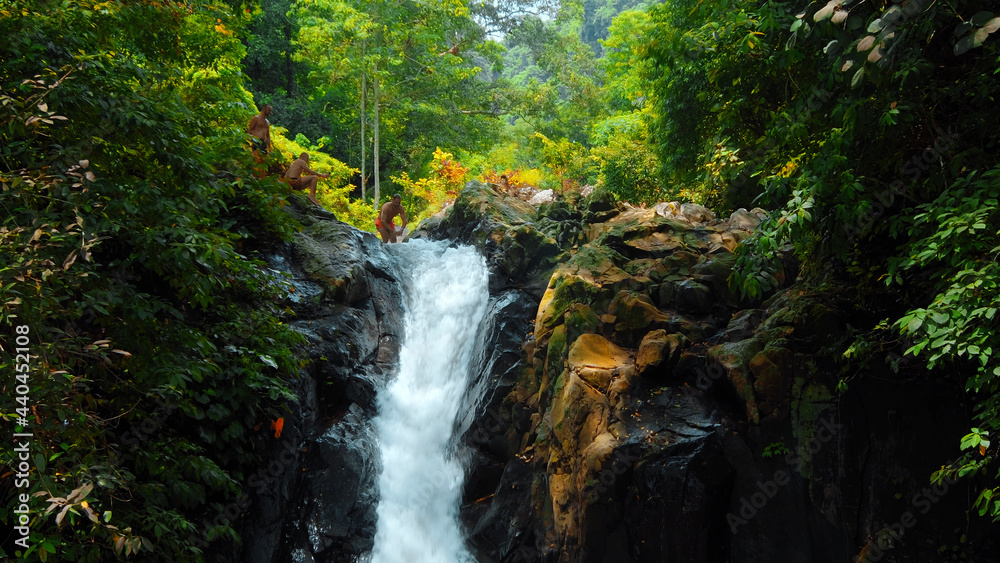 Picture of waterfall with rocks among tropical jungle with green plants and trees and water falling down