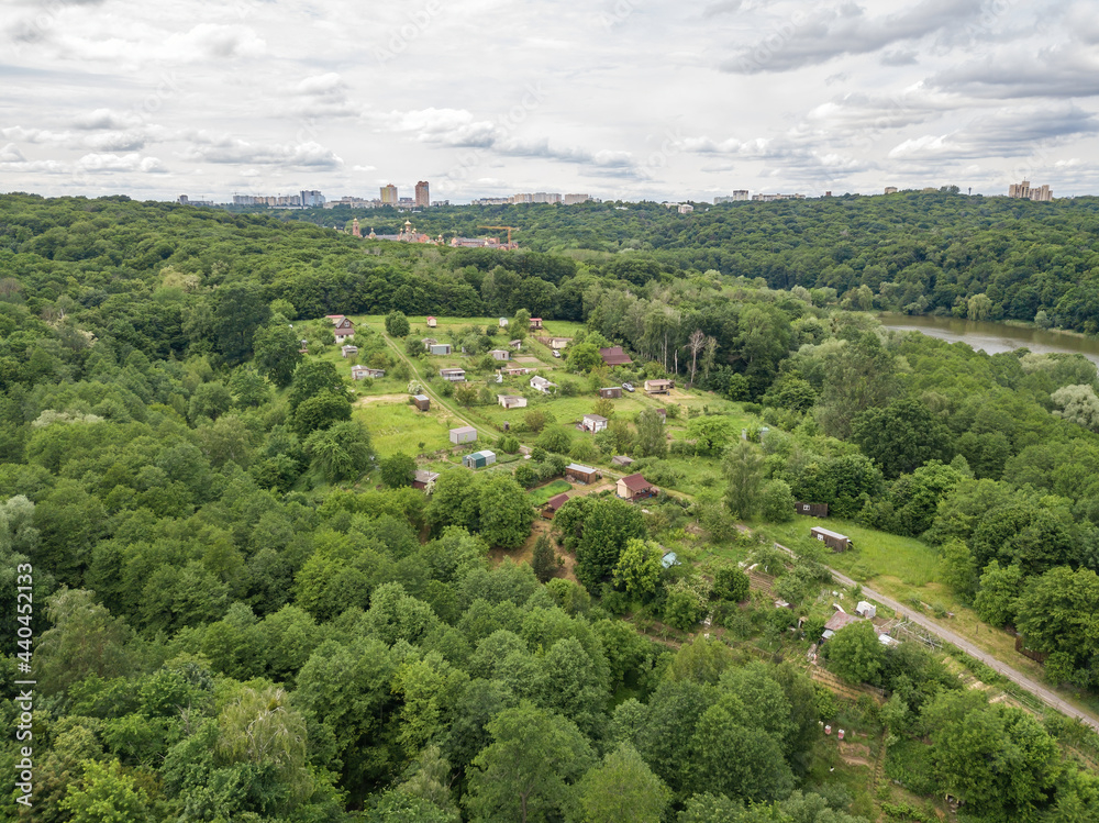 Low-rise settlement among green deciduous forest. Aerial drone view.