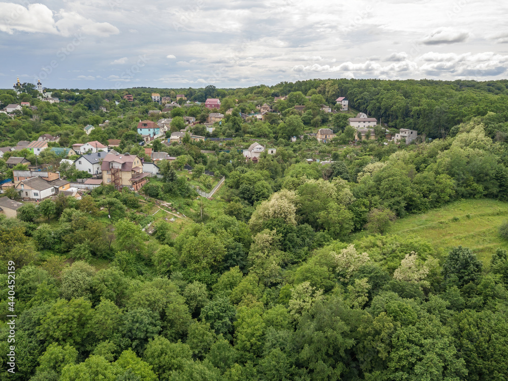 Low-rise settlement among green deciduous forest. Aerial drone view.