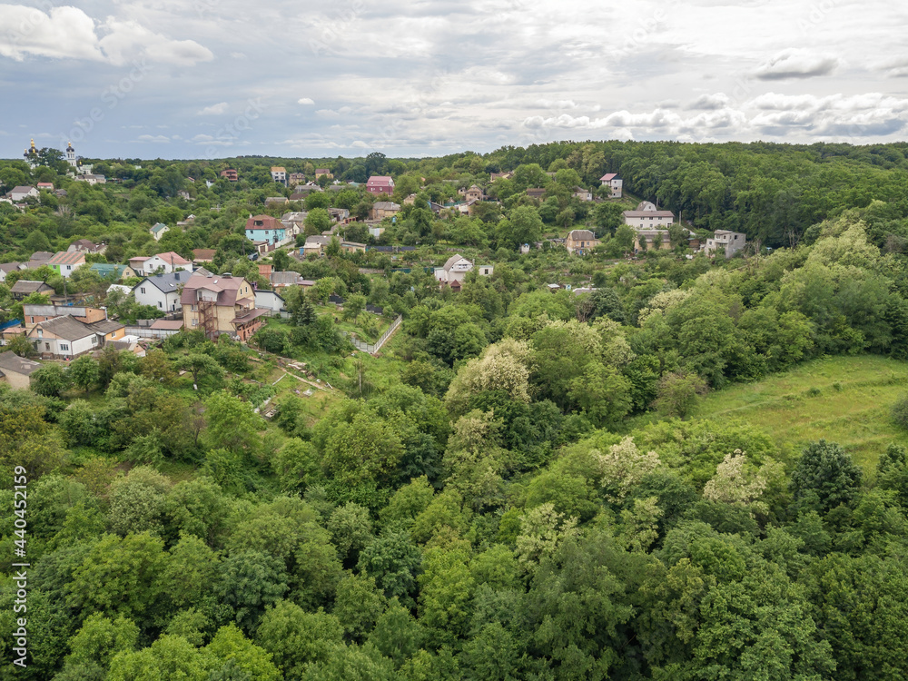 Fototapeta premium Low-rise settlement among green deciduous forest. Aerial drone view.