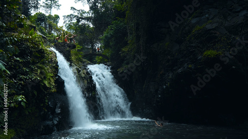 waterfall with rocks among tropical jungle with green plants and trees and water falling down into river