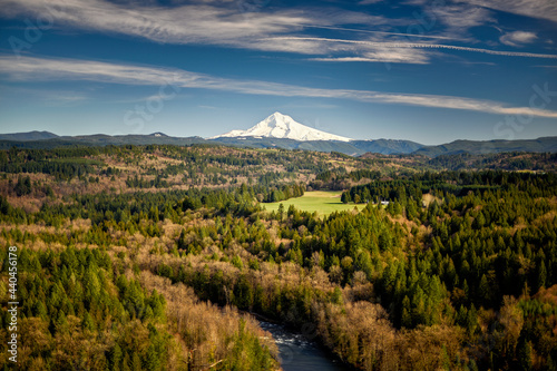 Landscape of Mt. Hood and blue sky and clouds with the Sandy River in the foreground along with a green and brown fall color forest.