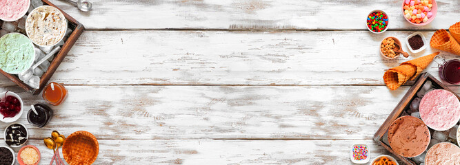 Summer ice cream buffet with an assortment of ice cream flavors and tasty toppings. Top view double border over a rustic white wood banner background.