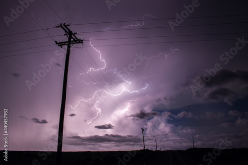 A powerful storm fills the night sky with lightning bolts, behind the silhouette of power lines.