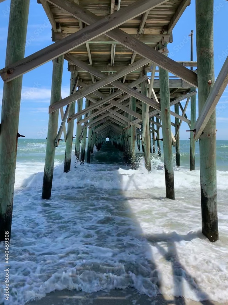 Underneath Wooden Ocean Pier over Clear Teal Water Crashing on Wooden Pillars