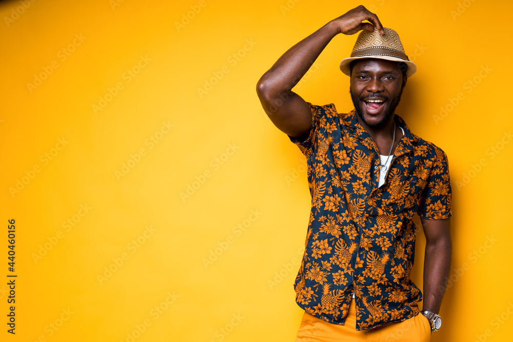 Cheerful african american man in a hat and in a colorful shirt smiles broadly touching his hat Cheerful african american man in a hat and in a colorful shirt smiles broadly touching his hat