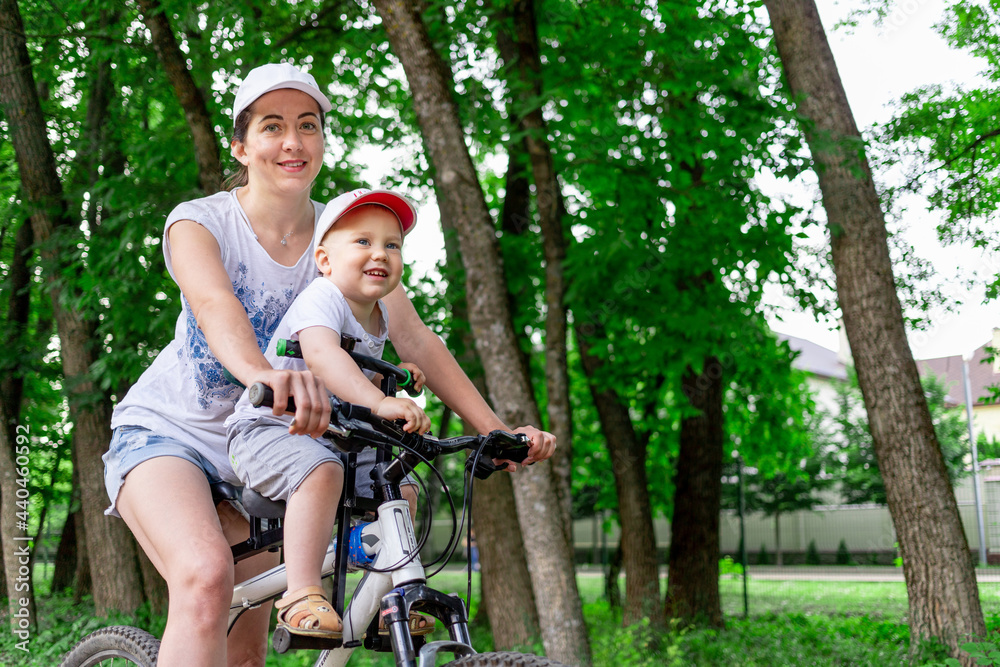 mother and son ride a Bicycle, mother carries a child in a child's chair on a Bicycle in the Park in the summer