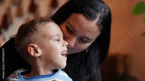 Close up portrait of a little boy with special needs and mom laughing at a table in a cafe, lifestyle. Mom's love for her child, inclusion.Happy disability kid concept